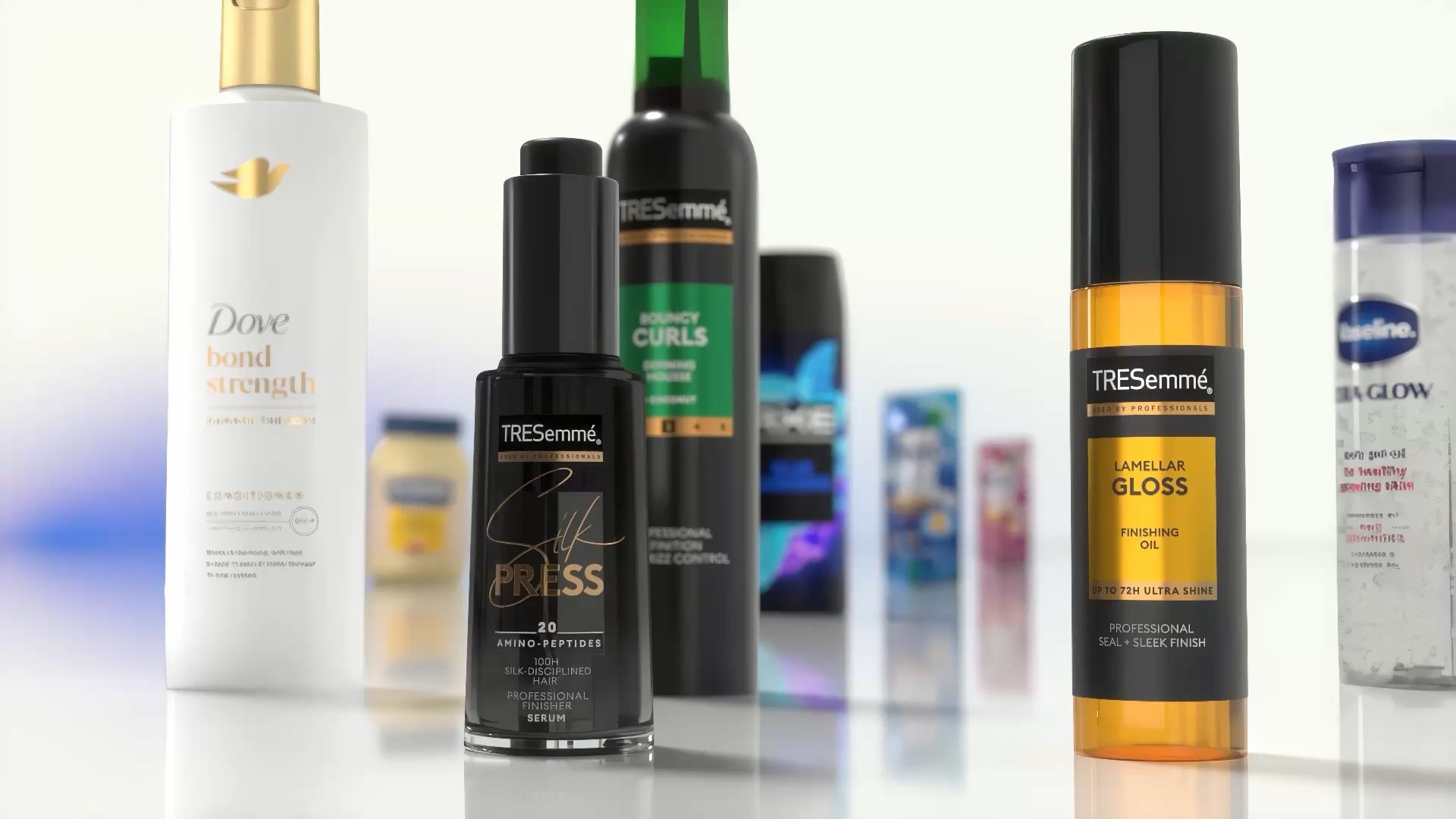 Primer plano de diversos productos para el cuidado del cabello y el cuerpo expuestos sobre una superficie reflectante. Entre los artículos visibles se encuentran el acondicionador Dove Bond Strength, el sérum TRESemmé Silk Press, el aceite de acabado TRESemmé Lamellar Gloss y otros productos de Unilever al fondo.